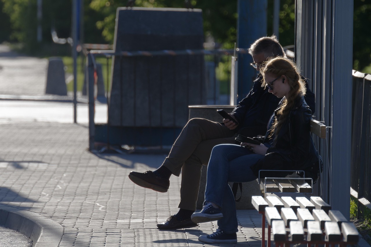 Two people sit on a bench at a bus stop.