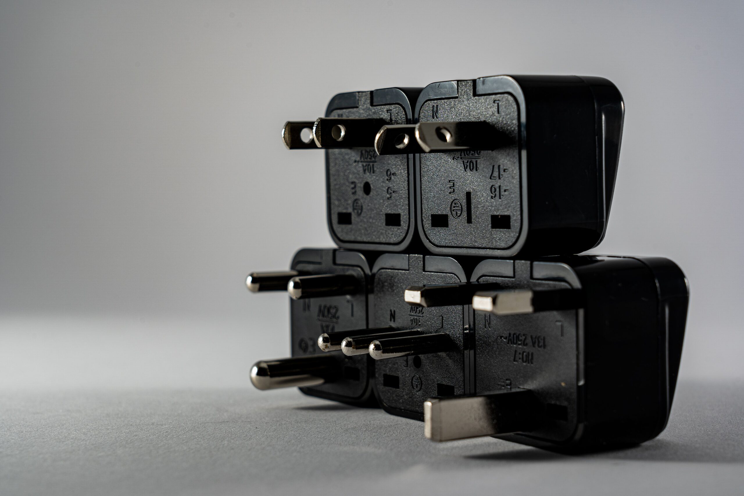 Black electrical adapters stacked on grey Black electrical adapters stacked with different plug ends facing forward
