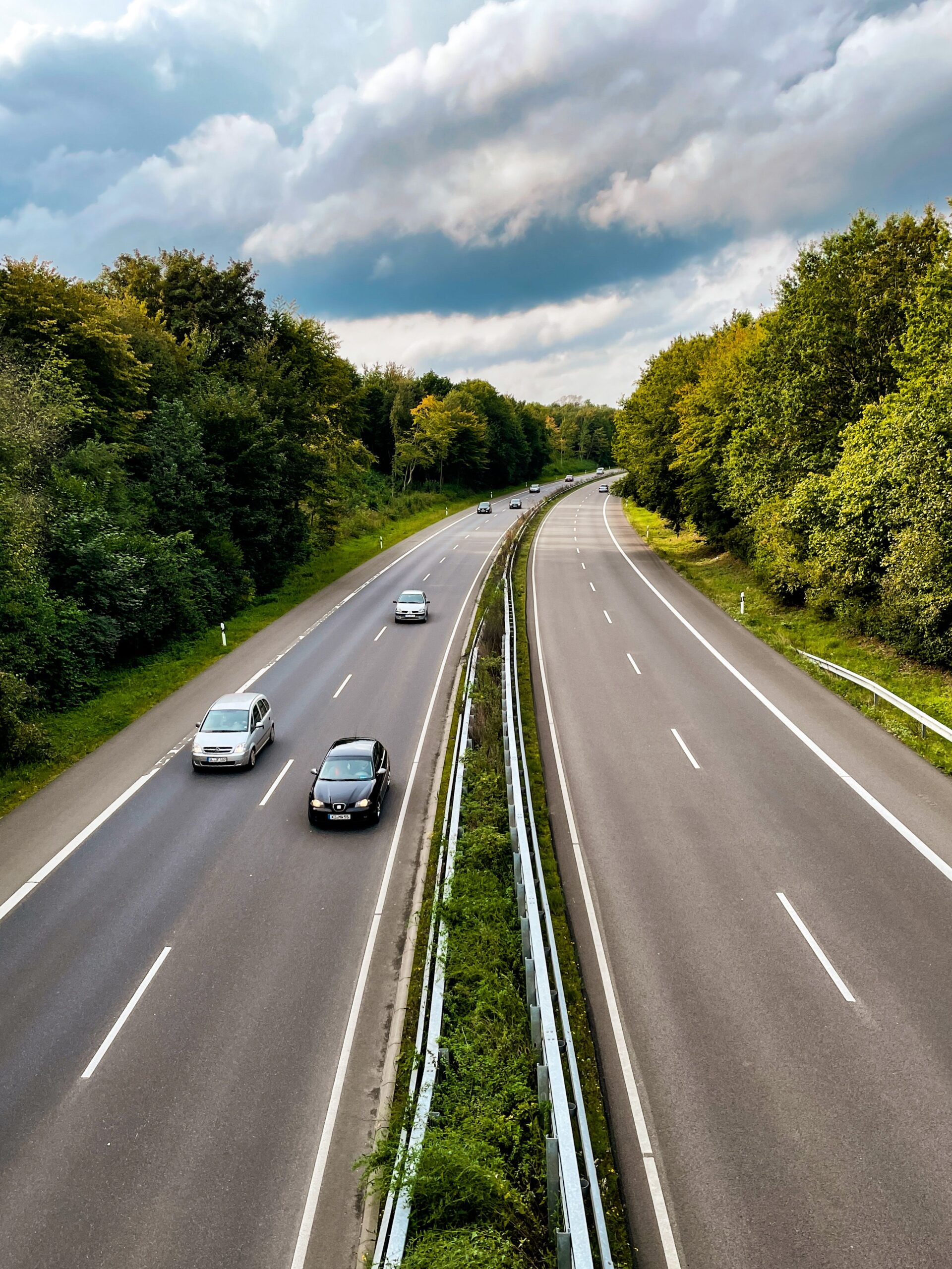 Cars travel along a divided, tree-lined highway.