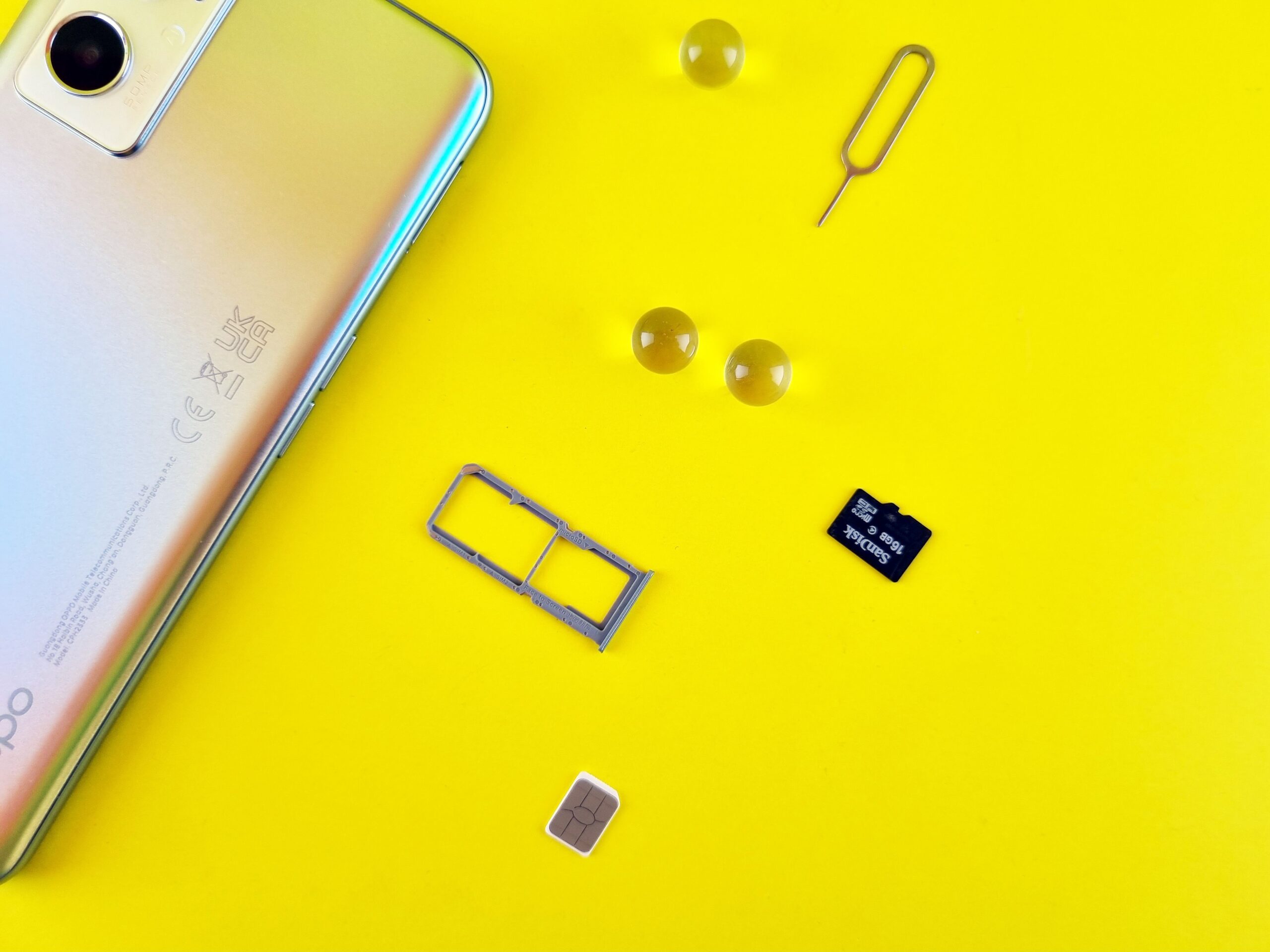 A smartphone beside its SIM tray, SIM card and memory card on a yellow surface