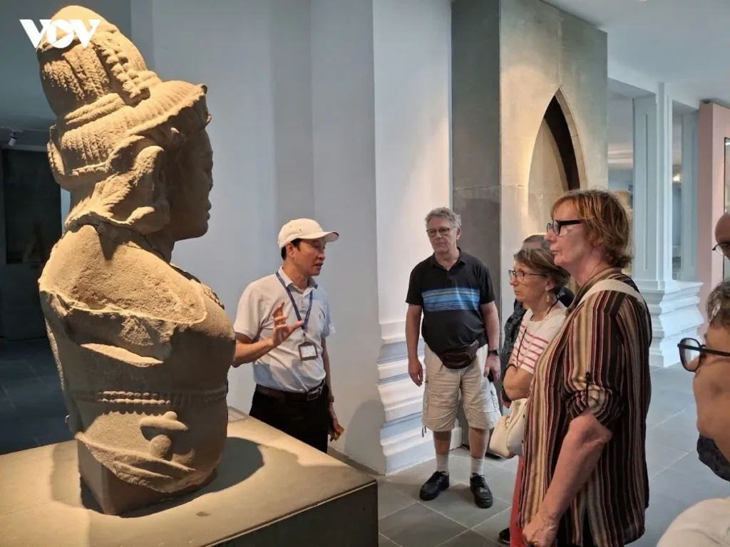 A guide gestures toward a Cham sculpture as visitors look on in the Da Nang Museum of Cham Sculpture.