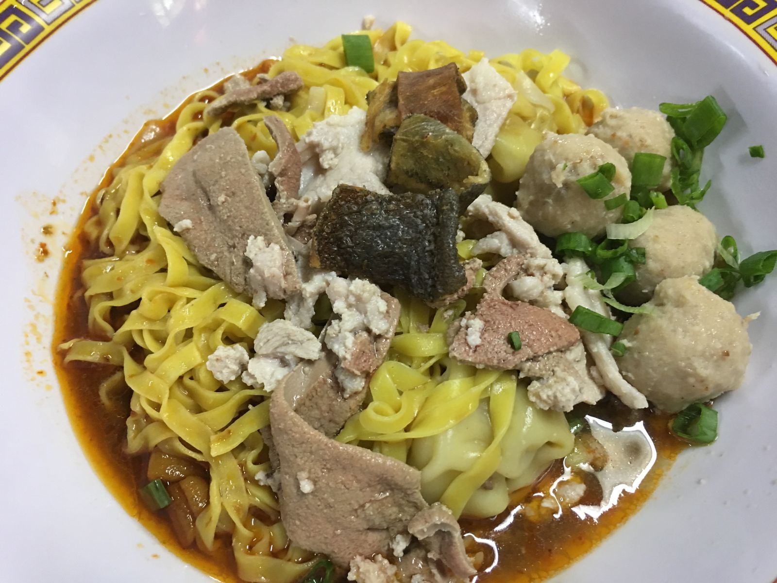 Bowl of noodles with sliced meat, meatballs and chopped green onion
