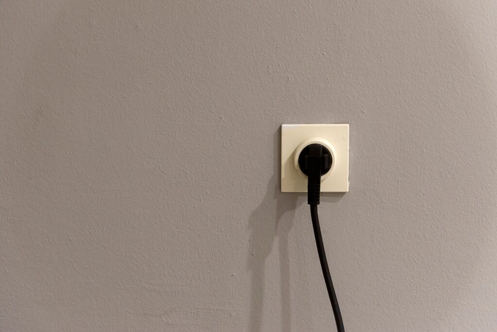 A black plug inserted into a white wall socket on a grey wall