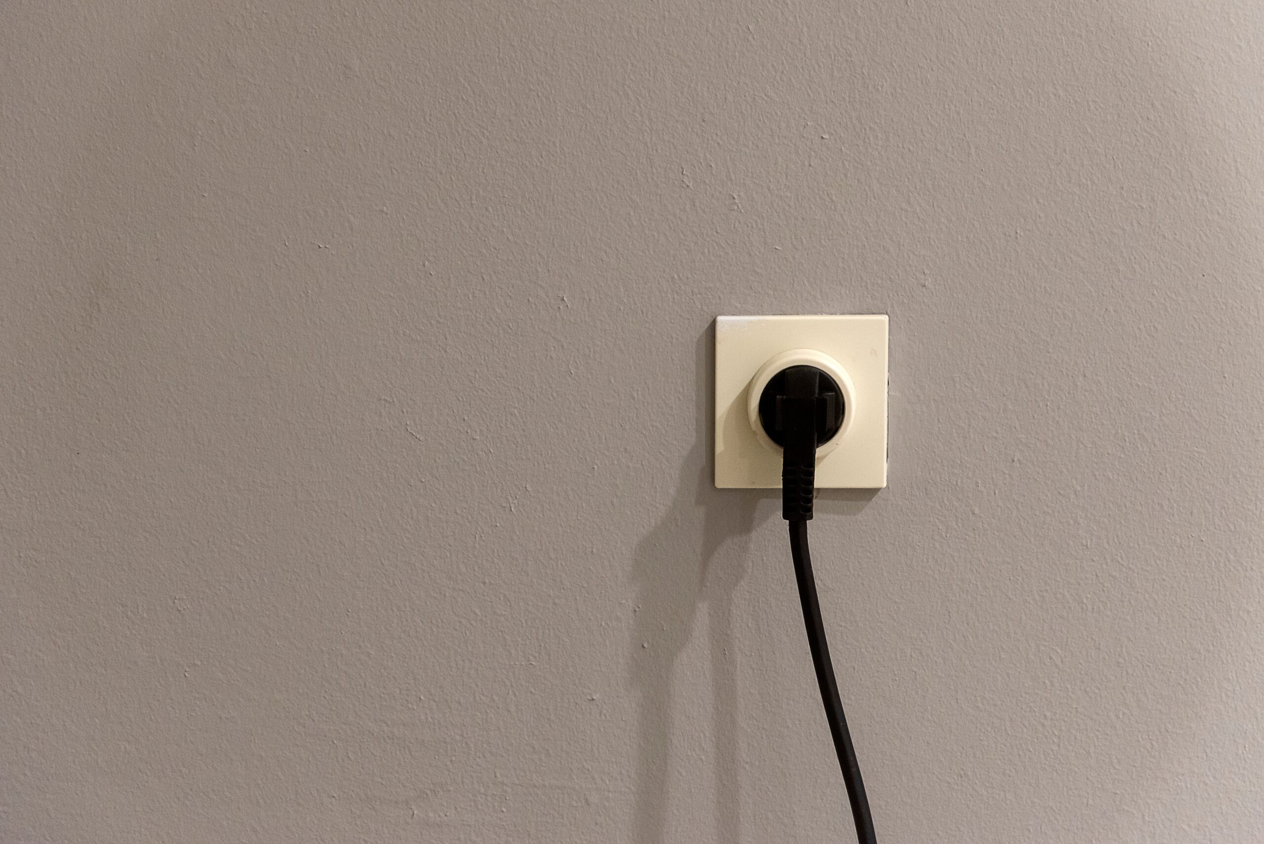 A black plug inserted into a white wall socket on a grey wall
