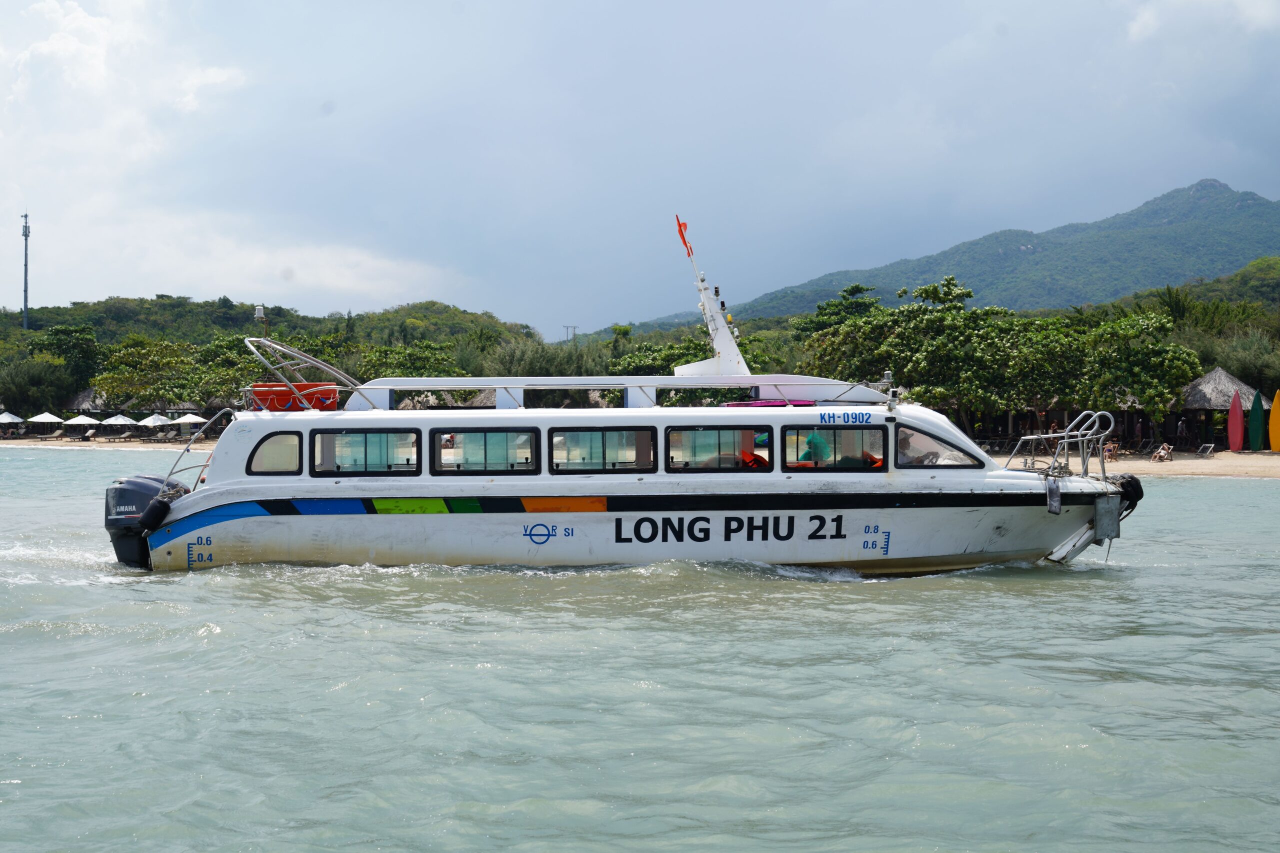 Small passenger boat moving beside a tropical coastline