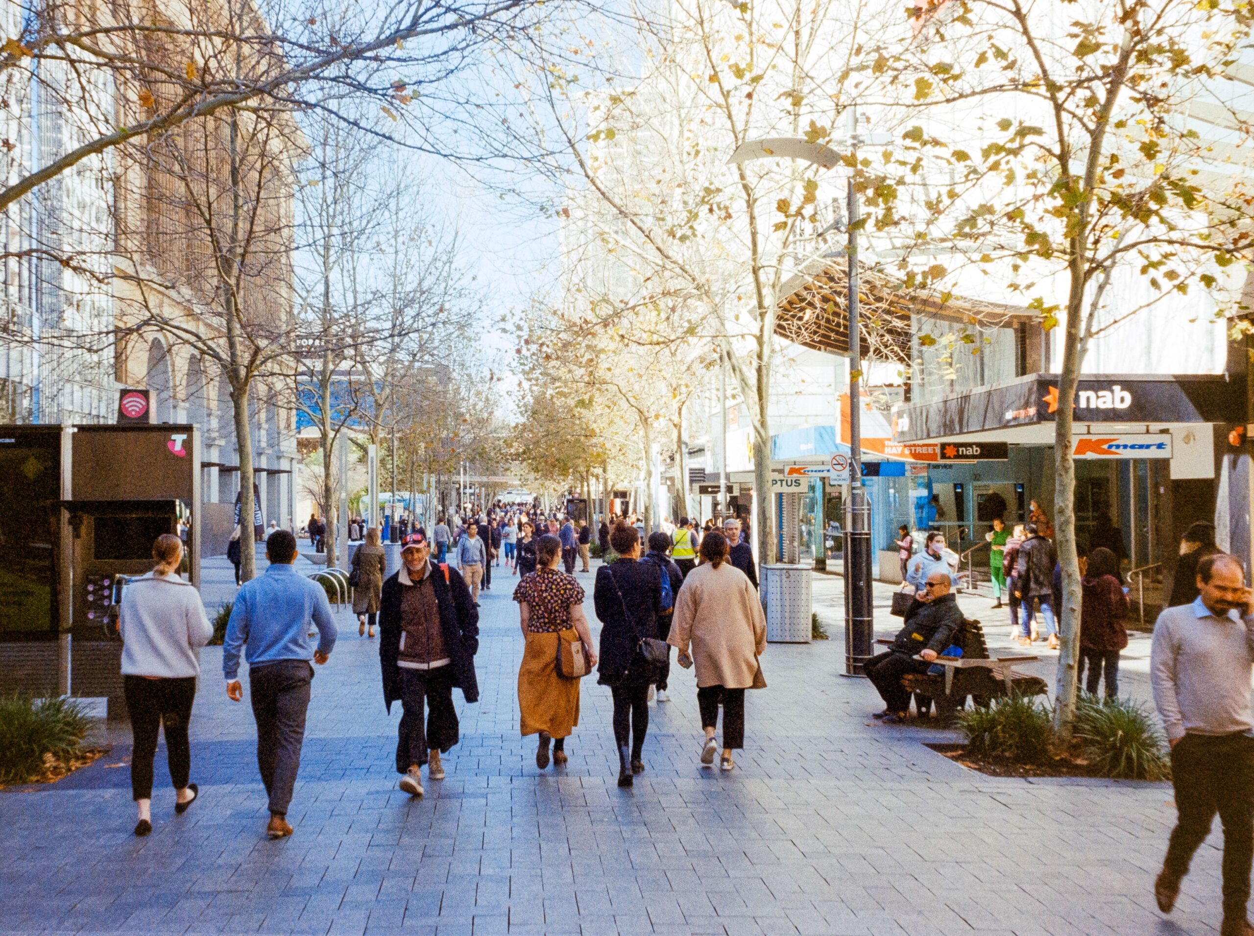 Pedestrians walking beneath trees along a Perth city shopping street