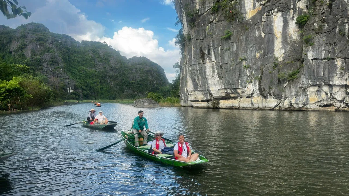 Guests on a sampan beside limestone cliffs in Tam Coc