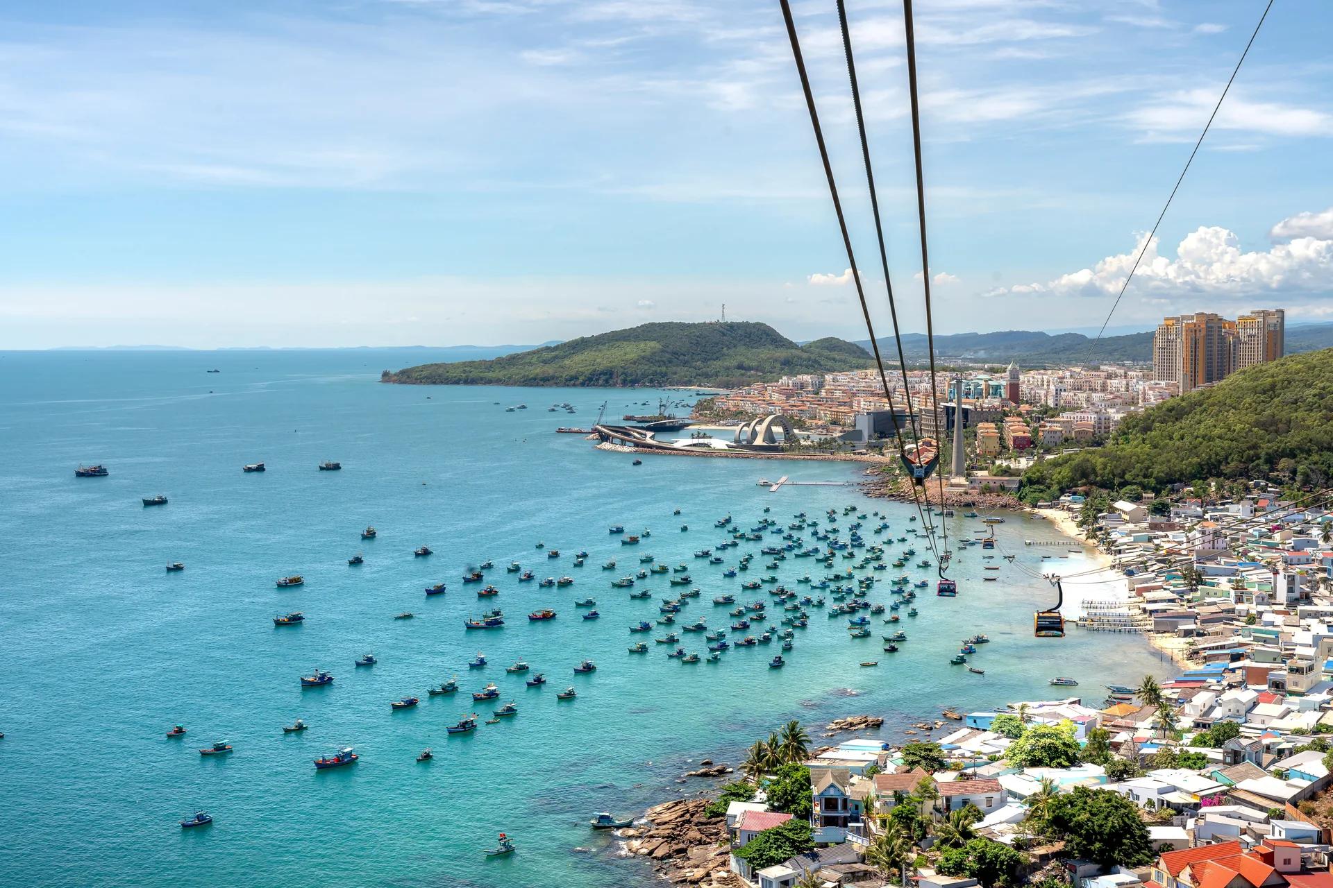 Aerial view of Phu Quoc bay with fishing boats, green coastline and cable cars crossing the water.