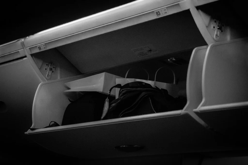 A suitcase and bag stored in an airplane overhead compartment.