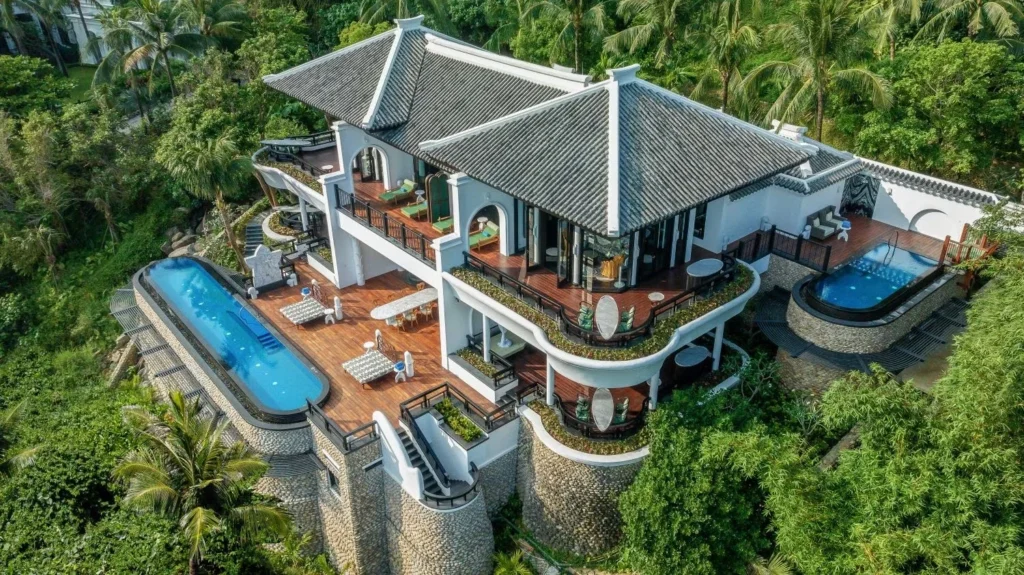 A multi-level villa with two swimming pools amid tropical greenery.