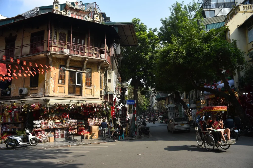 A cycle rickshaw passes a traditional storefront on a Hanoi street.
