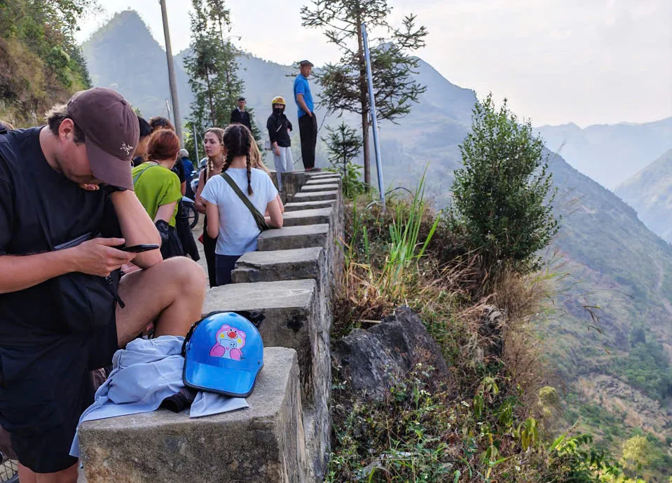 Visitors stand beside a concrete railing above a steep mountain slope in Lung Cu.