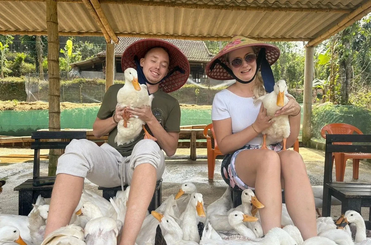 Two guests in conical hats holding white ducks at Duck Farm.