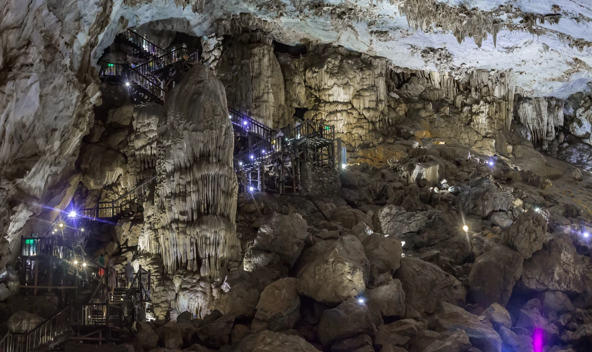 A winding illuminated boardwalk between towering limestone formations inside Paradise Cave.