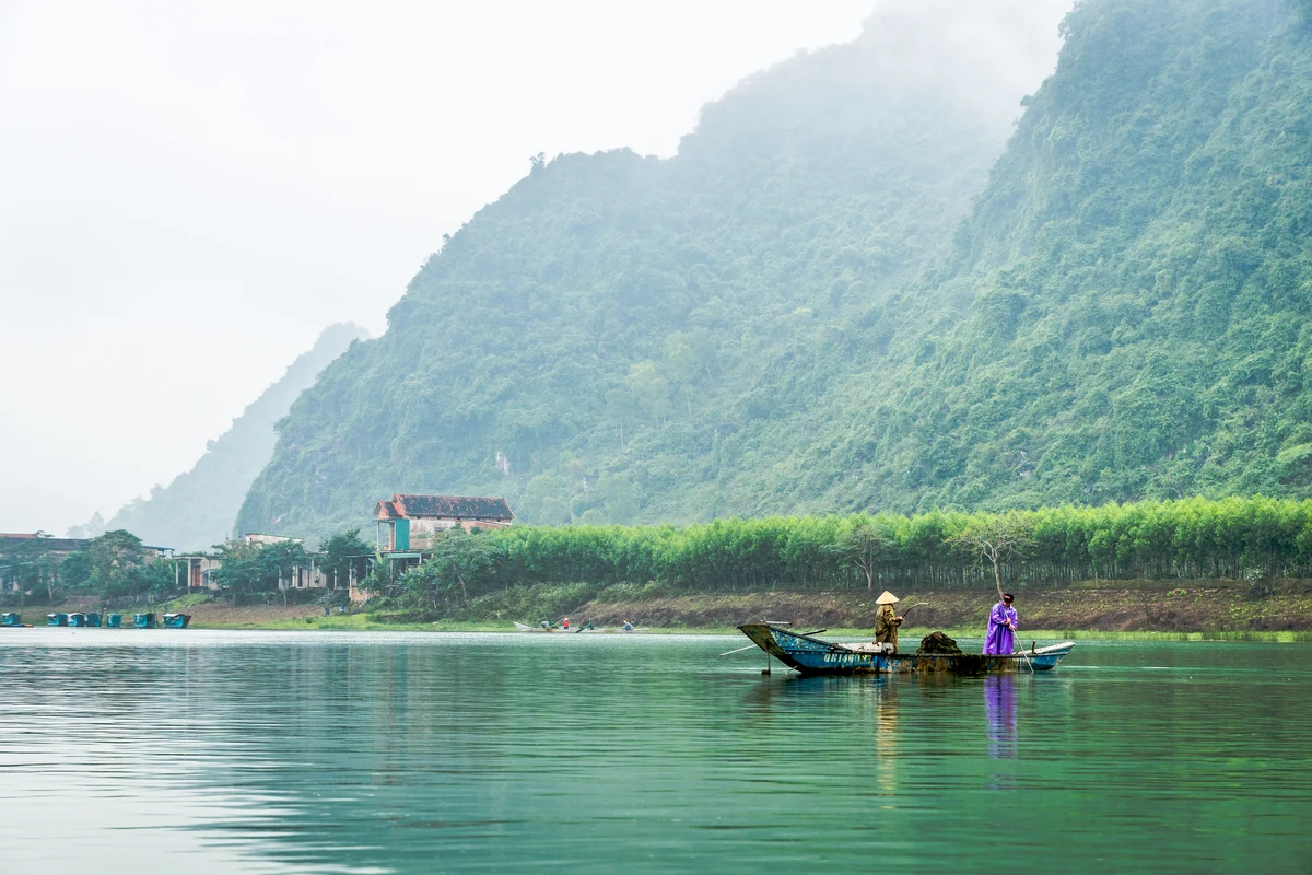 A small boat crossing calm water below green limestone mountains in the Phong Nha area.